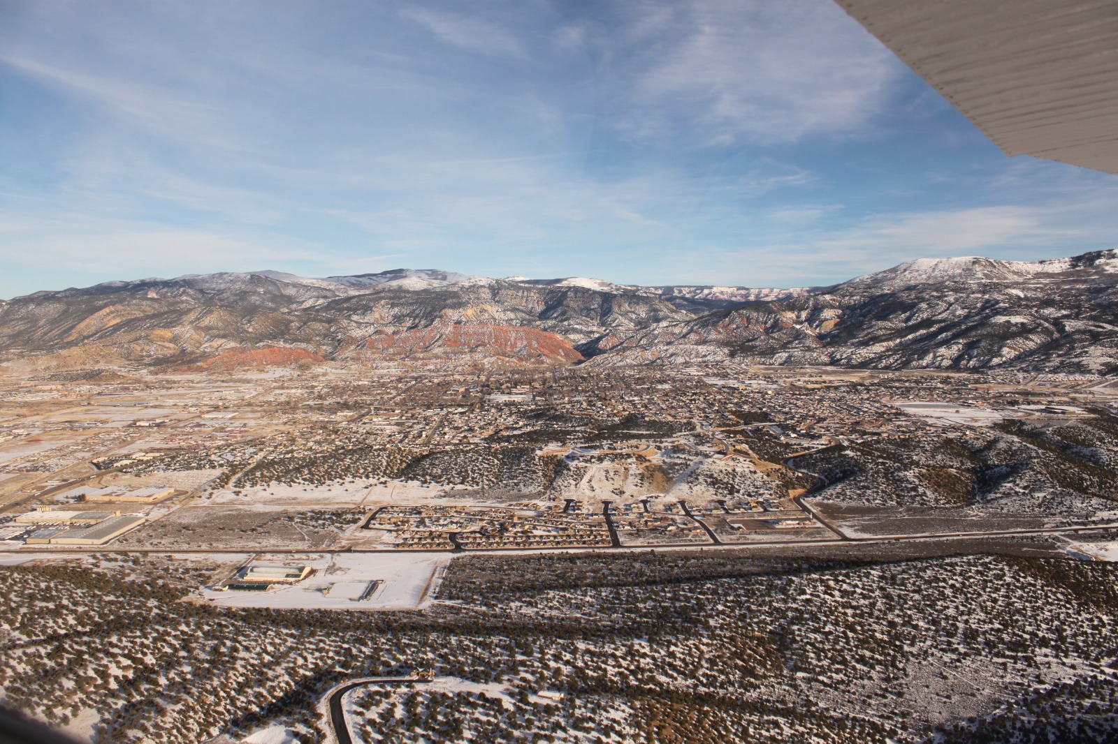 Snow-covered town with surrounding mountains and red rock formations, viewed from above